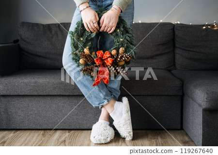 Person holding handmade Christmas wreath with pinecones and red bow, standing in cozy home setting. DIY holiday decor, festive minimalism, and winter crafts. Person holding handmade Christmas wreath with pinecones and red bow, standing in cozy home setting. DIY holiday decor, festive minimalism, and winter crafts. 119267640