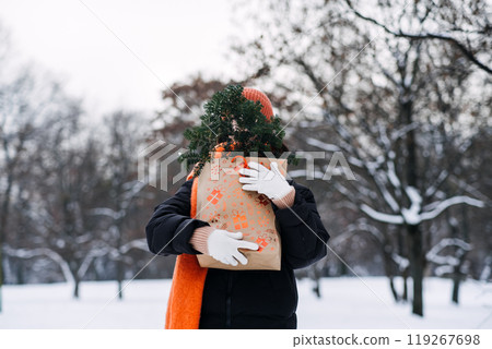 Person in a snowy park carrying a festive gift bag with evergreen branches, showcasing sustainable holiday shopping and natural seasonal decor. Person in a snowy park carrying a festive gift bag with evergreen branches, showcasing sustainable holiday shopping and natural seasonal decor. 119267698