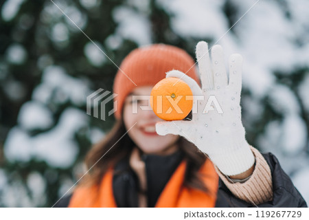 Close-up of woman holding an orange in a snowy outdoor scene. Winter immunity, fresh citrus, healthy living during cold season Close-up of woman holding an orange in a snowy outdoor scene. Winter immunity, fresh citrus, healthy living during cold season 119267729