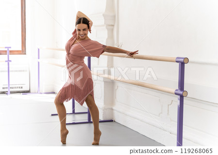 Elegant female dancer in rehearsal hall practicing ballet poses at barre Elegant female dancer in rehearsal hall practicing ballet poses at barre 119268065