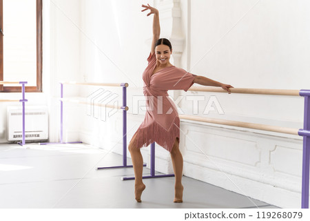 Beautiful woman practicing ballet at barre in studio wearing elegant dress 119268079