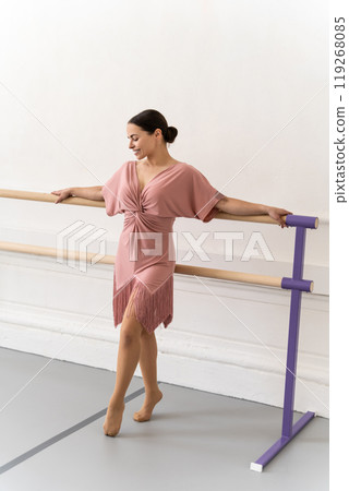 Ballerina standing on tiptoe and holding her hands on ballet barre in dance studio 119268085
