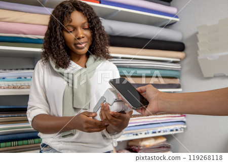 Shop assistant helps to shopper to complete purchase using contactless payment in fabric store Shop assistant helps to shopper to complete purchase using contactless payment in fabric store 119268118