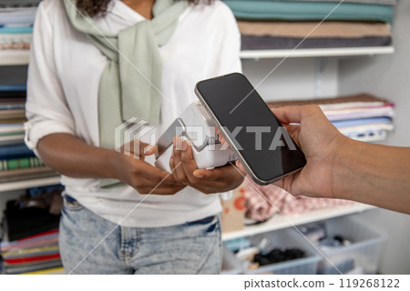 Unrecognizable woman shop assistance making payment with cell phone and customer Unrecognizable woman shop assistance making payment with cell phone and customer 119268122