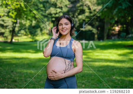 Pregnant woman practicing yoga listening to music through headphones 119268210