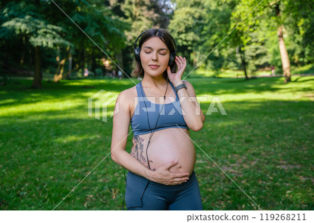 Sporty pregnant woman with headphones after sport workout in park 119268211
