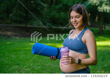 Pregnant woman practicing yoga during summer day holding water bottle 119268224