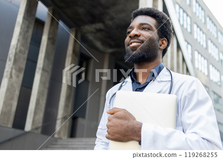 Doctor standing outdoors clinic holding laptop in one hand ready to connect with patients online 119268255