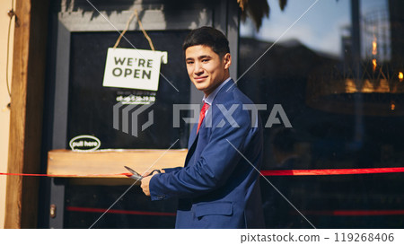 Confident businessman in blue suit, owner cutting red ribbon, symbolizing official launch and opening of new business ventures Confident businessman in blue suit, owner cutting red ribbon, symbolizing official launch and opening of new business ventures 119268406