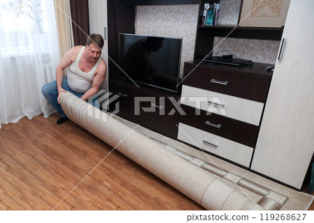 A man lays a carpet on the floor in his new apartment 119268627