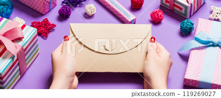 Top view of woman holding an envelope on purple background made of holiday decorations. Christmas time concept Top view of woman holding an envelope on purple background made of holiday decorations. Christmas time concept 119269027