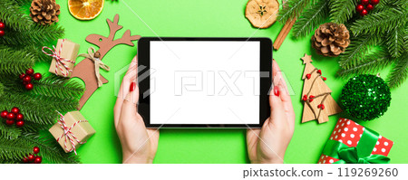 Top view of woman holding tablet in her hands on green background made of Christmas decorations. New Year holiday concept. Mockup Top view of woman holding tablet in her hands on green background made of Christmas decorations. New Year holiday concept. Mockup 119269260