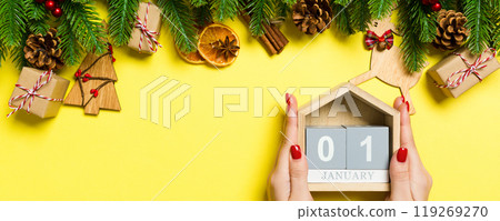 Top view of female hands holding calendar on yellow background. The first of January. Holiday decorations. New Year concept 119269270