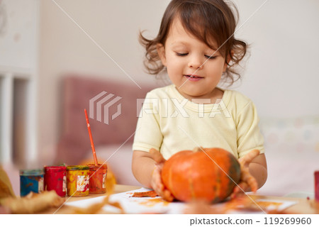 happy little child girl painting Halloween pumpkin. smiling baby girl drawing autumn pumpkin in yellow paint 119269960