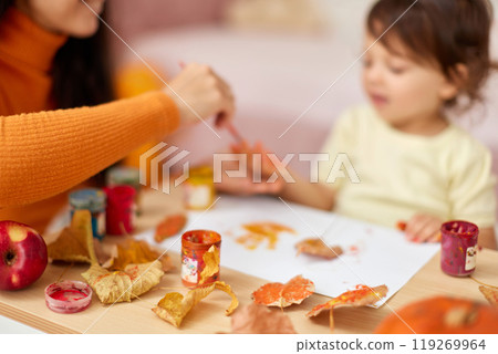close-up, child and mom hands painting autumn yellow leaves together. happy time together at home 119269964