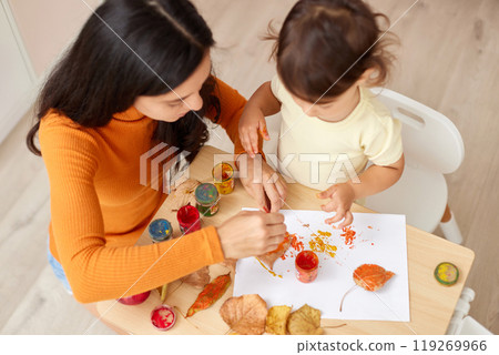 Cute little girl and mom spending good time painting autumn yellow leaves together 119269966