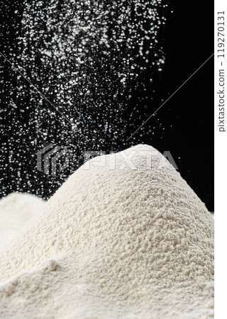 Wheat flour pouring onto a pile on a black background. 119270131