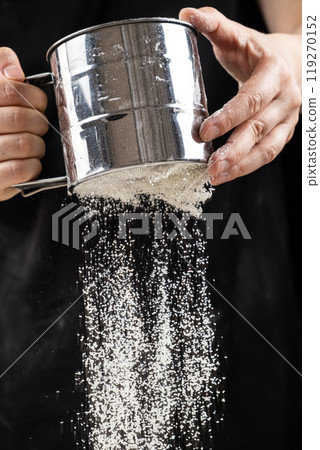 The cook sifts the wheat flour through a metal sieve. 119270152