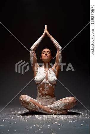 Woman Covered in White Paint Sitting in Lotus Pose 119270673