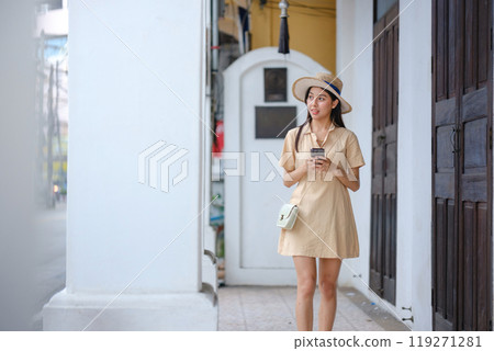 A woman in a yellow dress is walking down a street while holding a cell phone 119271281