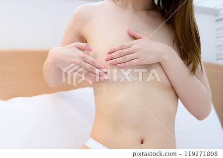 A woman in underwear applying body cream to her chest and stomach in bed Skin care Body care Bust care Trimming 119271808