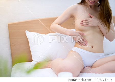 一位穿著內衣的年輕女子在床上塗抹身體霜，進行胸部和腹部的皮膚護理、身體護理、胸部護理。 119271827