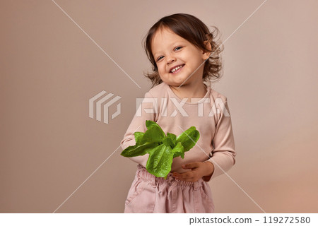 smiling child girl holding fresh green salad on beige background. healthy baby food. 119272580