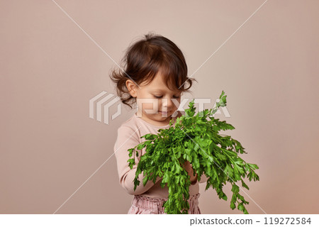 adorable child girl holding fresh green parsley on beige background. healthy baby food. 119272584