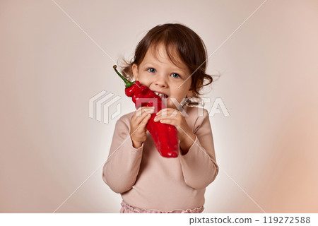 cute baby girl bites fresh red pepper on beige background. healthy baby food. kid loves vegetables 119272588