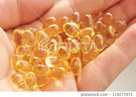 Golden capsules of omega-3 fish oil in hand for health and wellness supplements 119272971