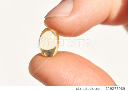 Close-up of hand holding yellow nutritional supplement capsule against white 119272989