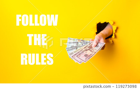A hand holding a stack of money with the words follow the rules written below it A hand holding a stack of money with the words follow the rules written below it 119273098