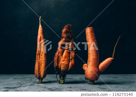 Three carrots are standing on a counter, one of which is bent and twisted 119273140