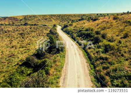 Drone view of the dirt road between hills on a sunny summer day 119273531