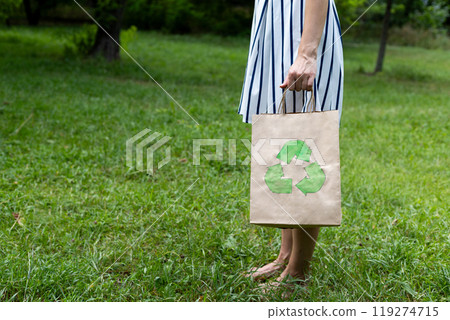 young woman holds an eco-package in her hands on the background of a green lawn, recycling young woman holds an eco-package in her hands on the background of a green lawn, recycling 119274715