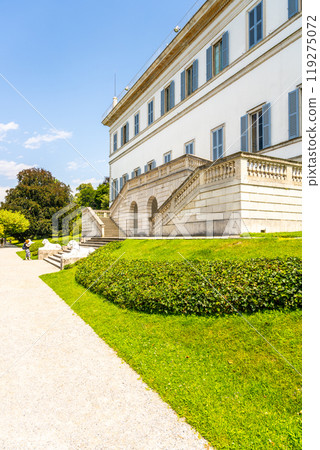 Visitors stroll through the lush gardens of Villa Melzi in Bellagio, enjoying the view of the neoclassical architecture against the serene backdrop of Lake Como on a sunny day. Visitors stroll through the lush gardens of Villa Melzi in Bellagio, enjoying the view of the neoclassical architecture against the serene backdrop of Lake Como on a sunny day. 119275072