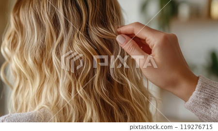 a close-up view of a person with soft, wavy blonde hair, while another hand gently holds and styles a section of the hair 119276715