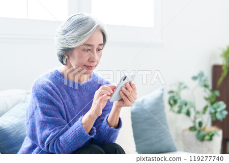 Middle-aged woman using a smartphone in the living room Middle-aged woman using a smartphone in the living room 119277740