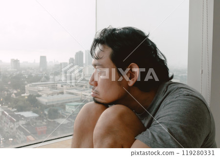 Introvert lonely man sitting hugging his knees looking out. 119280331