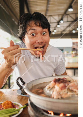 Happy and excited face man eating Moo Kra Ta or Thai BBQ buffet. 119280348