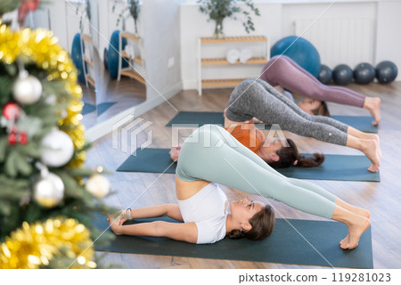 Girl teacher conducts lesson, training for girls in yoga studio and performs plow pose in New Year atmosphere 119281023