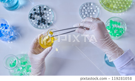Scene of a scientist's hand with medical gloves is taking a transparent gel ball out from a small erlenmeyer flask. Advertising photo was taken from top view Scene of a scientist's hand with medical gloves is taking a transparent gel ball out from a small erlenmeyer flask. Advertising photo was taken from top view 119281058
