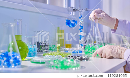 The promotional photo of experimental concept, a scientist is sits on the table by window and conducts experiment with colorful hydrogel balls. Side view, space for adding text 119281065