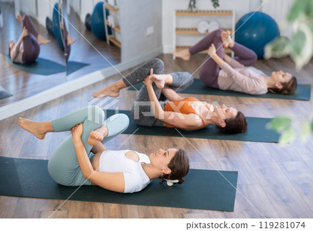 Girl teacher lead lesson, run training in female yoga studio and performs lying pigeon pose. Girl teacher lead lesson, run training in female yoga studio and performs lying pigeon pose. 119281074