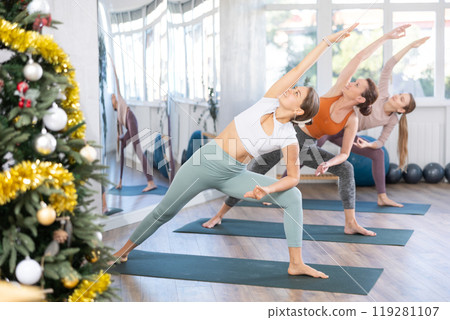 Woman performing Utthita Parsvakonasana in yoga studio decorated with Christmas tree Woman performing Utthita Parsvakonasana in yoga studio decorated with Christmas tree 119281107