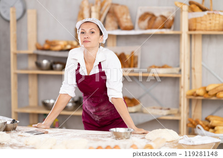 Portrait of successful young woman baker in apron smiling at camera posing during daily work in bakery 119281148