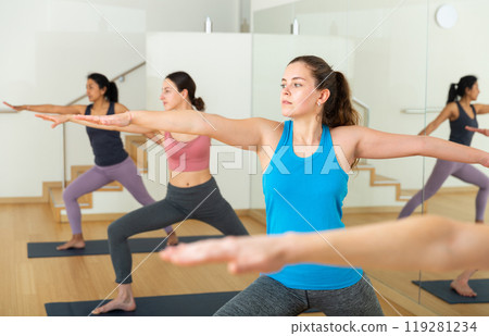 Girl practicing Virabhadrasana during group yoga training Girl practicing Virabhadrasana during group yoga training 119281234