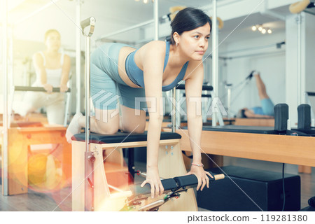 Young asian girl practicing pilates exercises on combo chair Young asian girl practicing pilates exercises on combo chair 119281380
