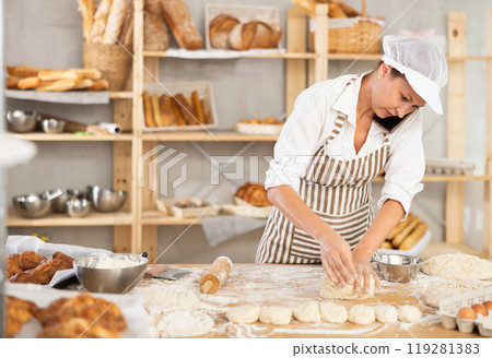 Female baker talking on phone while kneading dough in bakery 119281383