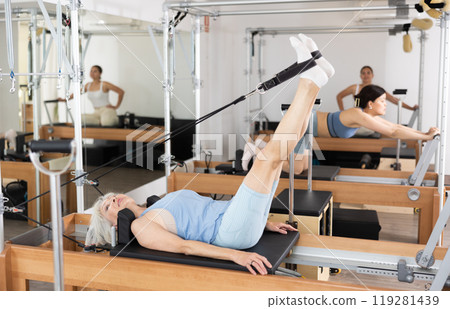 Elderly woman performing set of pilates exercises on reformer Elderly woman performing set of pilates exercises on reformer 119281439